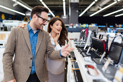 Beautiful and happy middle age couple buying consumer tech products in modern home tech store. They are choosing small kitchen appliances. People and consumerism concept.