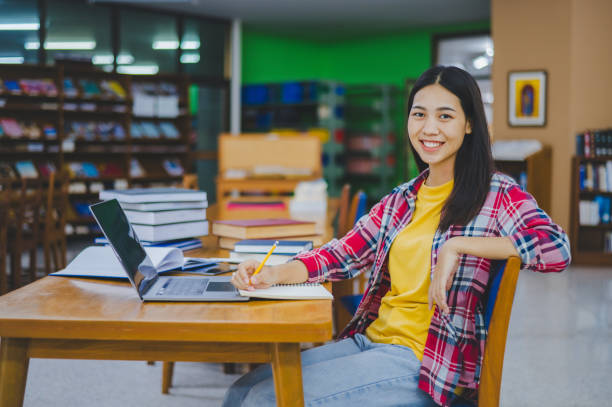 istock Smiling female student posing while working on laptop and searching for books to study, make report, find useful information in university room. 1682578798