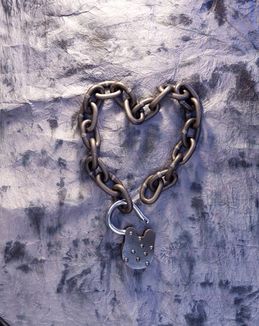 Five different colored heart shaped padlocks hanging from a chain in a row, light blue sky background, vertical