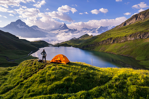 Rear view of hiker out of the camping tent admiring Bachalpsee lake at sunrise, Grindelwald, Bernese Oberland, Bern Canton, Switzerland