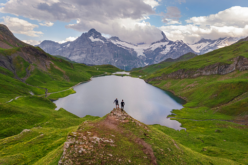 Happy hikers stand on top of a rock admiring the view around Bachalpsee at sunset, Grindelwald, Bernese Oberland, Bern Canton, Switzerland