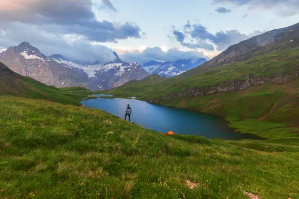 Hiker with tent stands on top of the Bachalpsee lake enjoying the amazing alpine landscape, Grindelwald, Bernese Oberland, Bern Canton, Switzerland