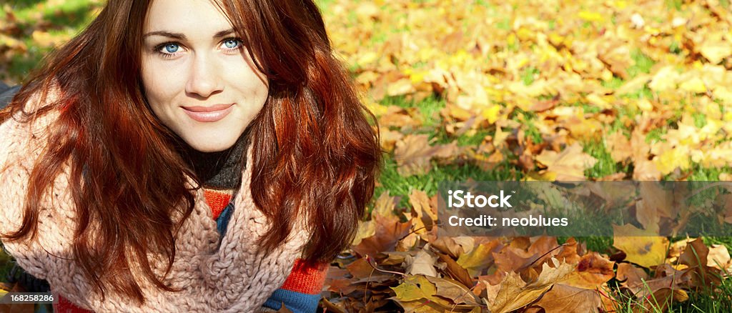 Woman with red hair laying on autumn leaves. Woman with red hair laying on autumn leaves. She has gloves and a multicolored sweater. Autumn Stock Photo