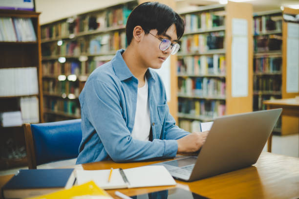 istock Male college students are working on laptops and searching for books to study, make reports, find useful information in college room. Concept of reading, learning and intelligence. 1682585292