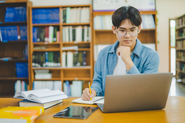 istock Male college students are working on laptops and searching for books to study, make reports, find useful information in college room. Concept of reading, learning and intelligence. 1682586221