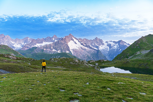 Hiker stands in the meadow in front of the massif of Mount Blanc close to the Lacs de Fenetre at dawn,  Ferret valley, Valais canton, Col du Grand-Saint-Bernard (St. Bernard mountain pass), Switzerland