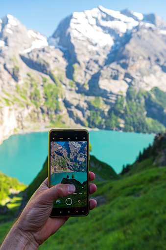 Perspective of a person taking photo with the smartphone at Oeschinensee lake, Bernese Oberland, Kandersteg, Canton of Bern, Switzerland