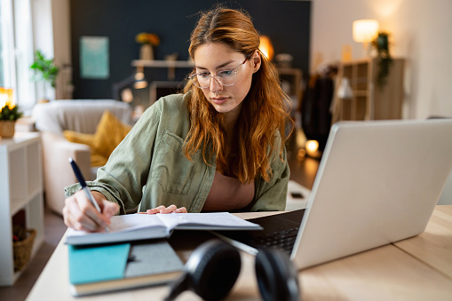 Young redhead Caucasian woman with vitiligo using laptop, while working or studying at home, enjoying the single life
