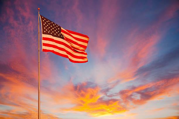 An orange and pink sunset surround the American Flag and makes it glow with pride.