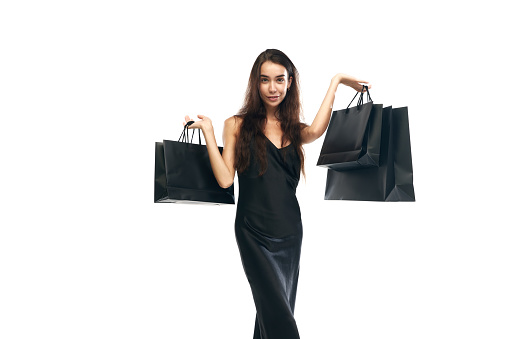 Portrait of beautiful woman wearing midi black dress raising hands with bags. Beginning season of sales. Concept of Black Friday, Cyber monday, fashion, buying, holiday shopping. Copy space for ad