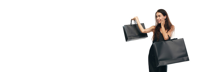 Portrait of beautiful woman wearing midi black dress raising hands with bags. Beginning season of sales. Concept of Black Friday, Cyber monday, fashion, buying, holiday shopping. Ad. Banner.