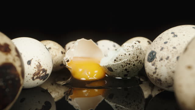 Quail eggs on a black table and background, one of them is cracked and spilled on the table. Dolly slider extreme close-up.