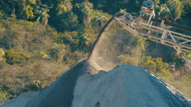 sand falling off conveyor belt, tilt up movement, wide shot, sunny sand quarry