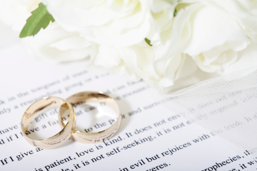 Wedding rings and bridal bouquet on a bible reading about love from Corinthians