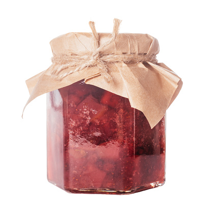 Close-up of glass jar full of delicious red lingonberry cowberry bearberry red bilberry whortleberry foxberry huckleberry pear jam with lid wrapped in beige craft paper on white background. Isolated.