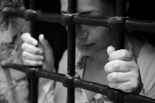 A young woman looking somber while holding onto prison bars. Focus on hand in foreground. Photographed in Syria (staged photo, not really a prisoner).