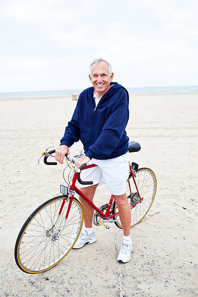 sênior homem posando com sua bicicleta, ao lado da praia - 65 70 age - fotografias e filmes do acervo