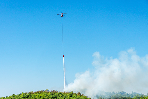 tragic view of forest fire and helibucket which  is a specialized bucket suspended on a cable carried by a helicopter to deliver water for aerial firefighting
