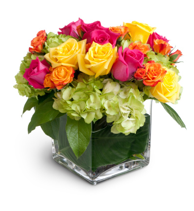 Vibrant multicolored flowers in a clear square crystal vase, isolated over a white background with cast shadow. Pink,yellow and orange roses are arranged with green hydrangea. Canon 5D MarkII.