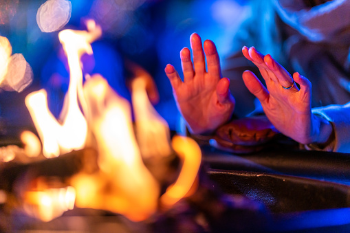 A woman enjoying the Montreal Christmas market at night and warming her hands near a fire pit.