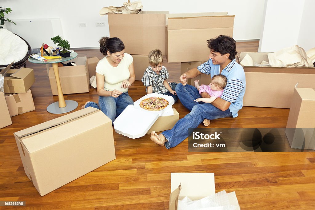 Giovane famiglia con due bambini mangiando pizza nel nuovo appartamento - Foto stock royalty-free di Famiglia