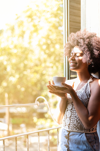 Vertical photo of an afrian american woman enjoying a coffee in the morning standing on the balcony