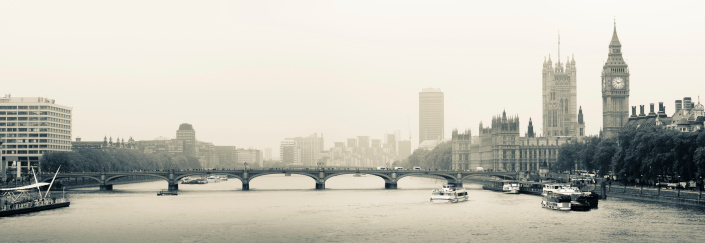 This aerial black and white photograph presents a timeless view over London's iconic skyline. Dominating the scene is the majestic silhouette of the Houses of Parliament and the iconic clock tower, Big Ben, standing as sentinels over the River Thames. The river's calm waters reflect the grandeur of these historical structures, while the sprawling urban landscape stretches into the horizon, peppered with both modern and ancient buildings. The overcast sky casts a diffuse light, lending the city a soft, ethereal quality and highlighting the intricate gothic architecture. This image encapsulates the enduring legacy and the unchanging face of London amidst the ever-evolving tapestry of city life, inviting the viewer to ponder the stories and history woven into the fabric of this grand metropolis.