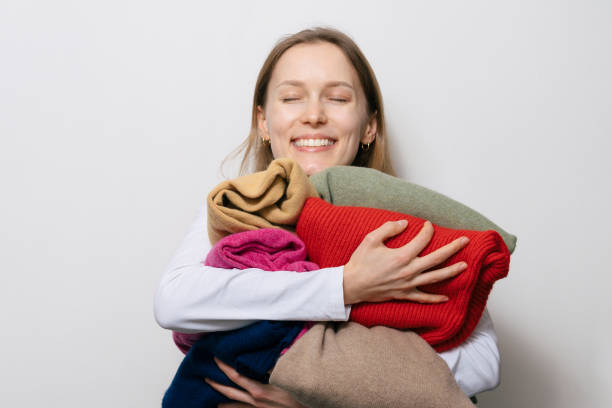 Kobieta uśmiecha się, trzymając stertę złożonych wełnianych swetrów, podkreślając dbałość i miłość do wełnianych ubrań.