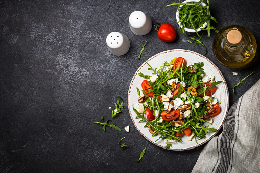 Arugula salad with tomatoes, blue cheese and walnuts. Healthy vegetarian dish. Top view image.