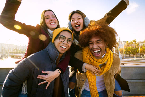 Group of multi-ethnic cheerful happy friends smiling at camera having fun outdoors. Boys carrying girls on back.