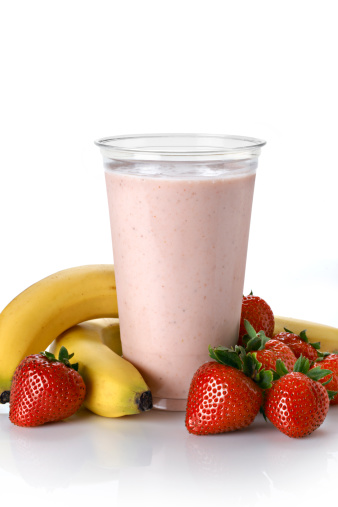 Strawberry and Banana fruit smoothie in a plastic take-away or disposable cup. White background with natural refection. Smoothie surrounded by fresh fruit. Made with fresh frozen fruit and fruit juice, yogurt can be added.
