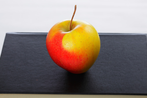 Red and yellow apple on black book closeup photo
