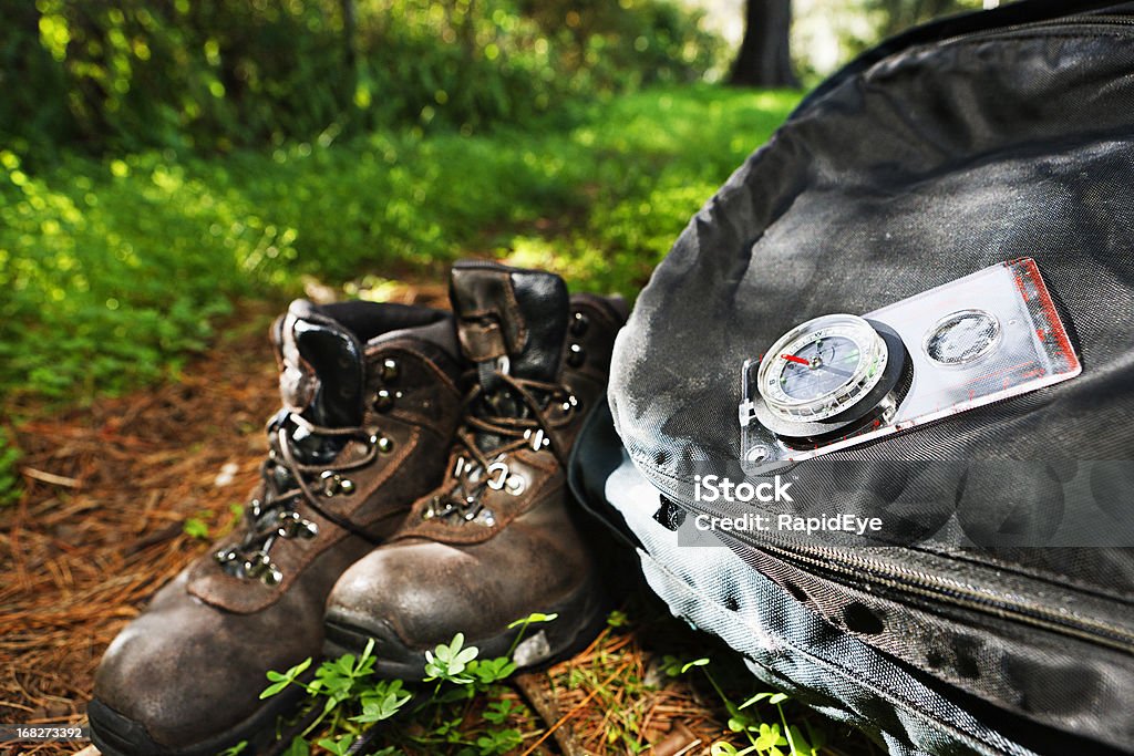 Hiking theme: boots, backpack and compass on sunlit forest path Hiking theme: compass, boots and backpack resting on a forest path. Camping Stock Photo