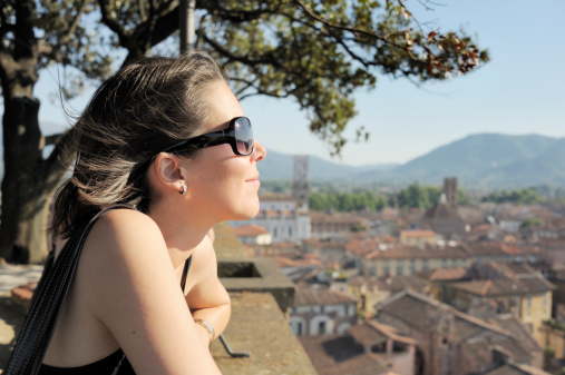 A charming young female tourist admires the view from the roof of the Torre dei Guinigi (Guinigi Tower) in Lucca, Italy. The 44 metre high tower-somewhat unusually-has trees growing on its roof.