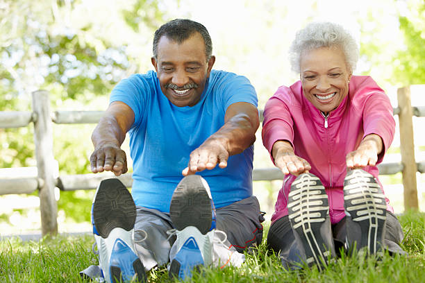 Senior African American Couple Exercising In Park Senior African American Couple Exercising In Park Stretching To Touch Toes touching toes stock pictures, royalty-free photos & images