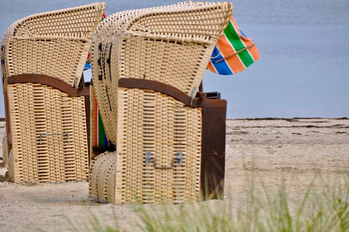 Three plastic adirondack chairs rest in the sand overlooking Cape Cod Bay in Massachusetts.