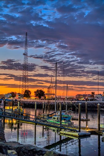 A colorful sunset illuminates the waterfront area, with an array of boats docked in the harbor