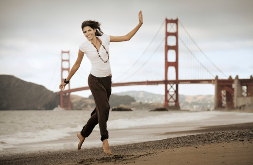 Beautiful natural model in a playful mid-air pose on Baker Beach in front of the Golden Gate Bridge. Nikon D3X + Sepia Filter to underline the mood and location. Converted from RAW.