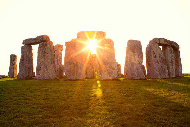 Dramatic Sunset at Stonehenge Horizontal Close-up view of ancient stones during sunset at UNESCO World Heritage Site at Stonehenge, Wiltshire, UK. Sun shines through the stones. Major tourist destination, archeological and pilgrimage site during Summer Solstice and Winter Solstice. Visible grain, softer focus. summer solstice stock pictures, royalty-free photos & images