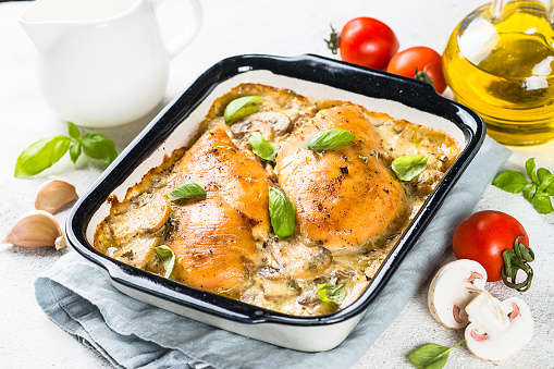 Baked chicken breast with mushrooms in cream sauce on white kitchen table.