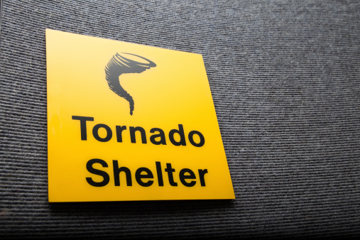 Yellow and black tornado shelter sign in an airport men's washroom entrance seen from close up.