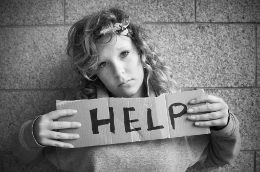 Young female teenager with a sign asking for help.