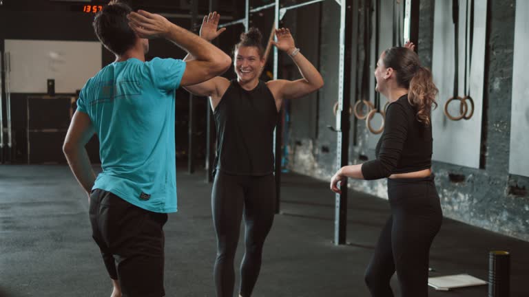 Cheerful female personal trainer winning and greeting athlete happy clients after successful fitness training in the gym