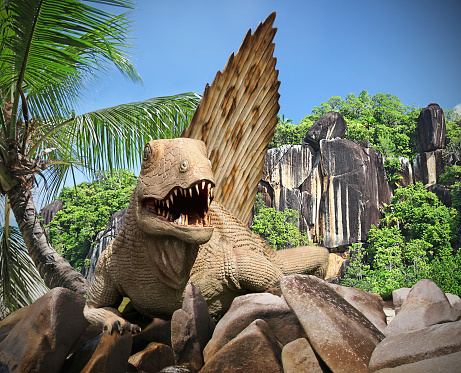 Fun get away from it all Jurassic concept, digitally created with a dinosaur scrambling over Rocks against stunning background of a deserted island in the indian Ocean