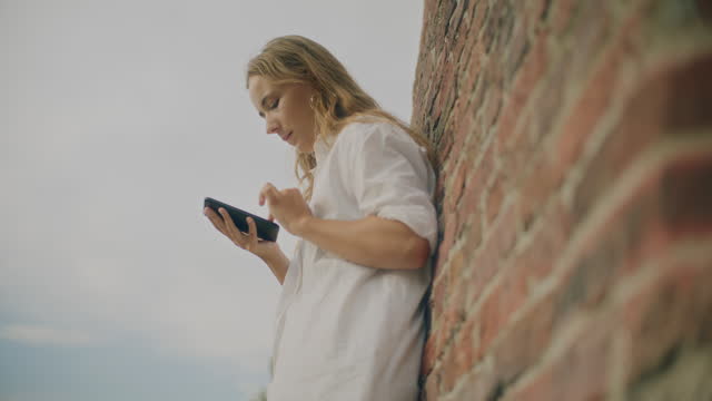 Woman Scrolling Smart Phone Leaning On Brick Wall