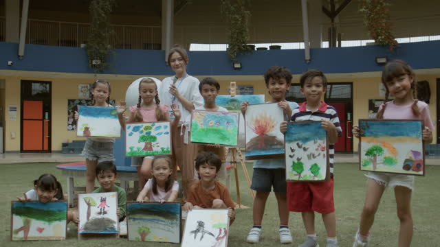 Portrait group of  student  and their teacher show paint board outdoors in school garden.
