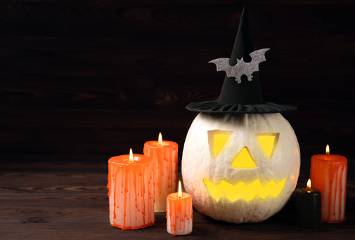 Halloween pumpkin on brown wood texture with candles. Composition on a dark background. Scary composition with glowing eyes and mouth. Holiday concept. copy space