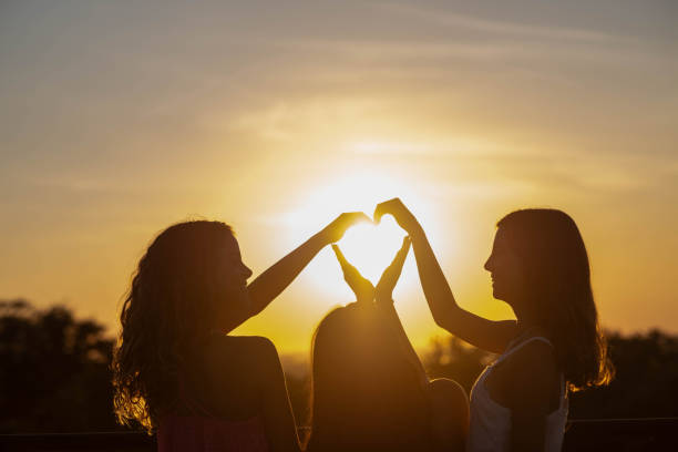 istock three girls make a heart shape with their hands at sunset 1682941798