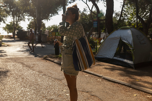 While going to the beach, a woman passes through a camp. She is carrying a stainless steel water bottle in her hands