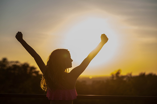 girl with raised arms standing outside at sunset